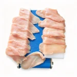 Latin worker operating horizontal chicken slicer, fresh chicken fillet slicing workshop scene